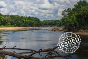 river running through a green forest, issued badge overlayed
